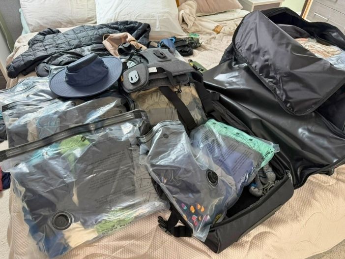 Camera gear and folded clothing laid out during final packing for a three-week trip
